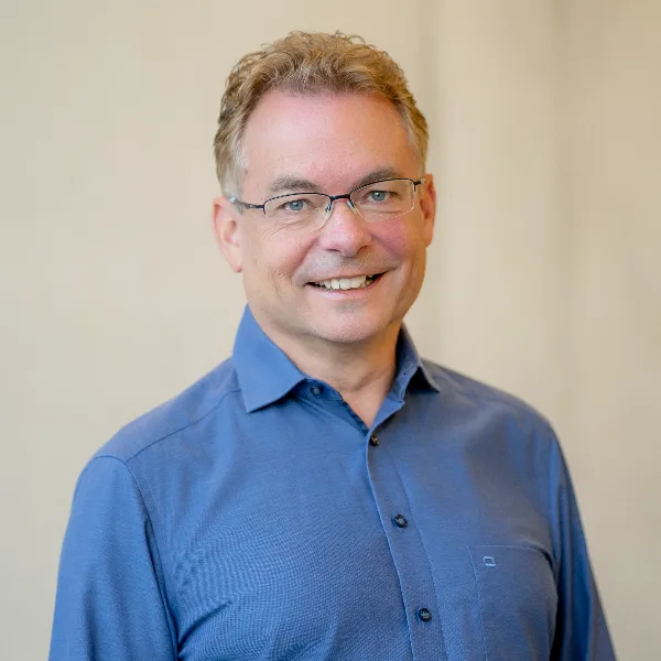 Ansprechpartner Gerd Otterbach Porträt eines lächelnden Geschäftsmanns mit Brille, Anzug und hellem Hintergrund.